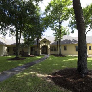 A single-story house with a well-maintained front yard, surrounded by trees and featuring a paved pathway leading to the entrance.