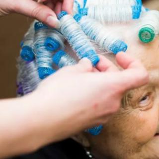 An elderly person getting their hair styled with curlers at a salon.