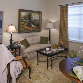 A cozy living room with elegant furniture and decor, featuring a sofa, coffee table, artwork on the wall, and warm lighting.