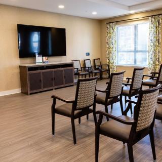 A well-lit conference room with rows of chairs facing a large television.