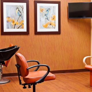 A cozy salon interior with orange chairs, wall art, and a television.