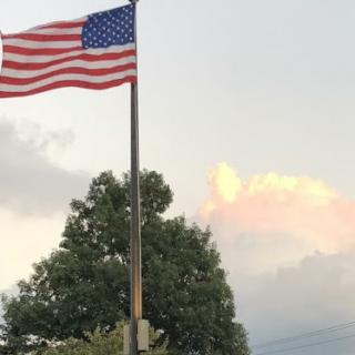 A United States flag waving against a backdrop of clouds during the evening.
