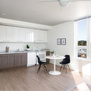 A modern and minimalist kitchen with a dining area, featuring white cabinets and natural lighting.