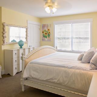 A cozy bedroom with a white bed, dresser, and mirror in a softly lit space.
