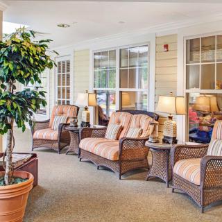 A cozy indoor seating area with wicker furniture and potted plants, illuminated by table lamps.