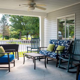A cozy porch with comfortable seating and a table, perfect for a relaxing sunny day.