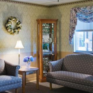 A cozy living room featuring a sofa and armchair, illuminated by a standing lamp with decorative elements like a wreath and floral curtains.