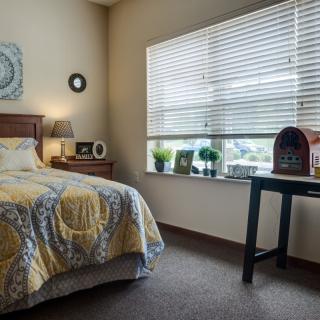 A cozy bedroom with a bed, nightstand, and window bringing in natural light.