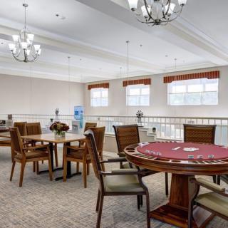 A well-lit dining area with multiple tables and chairs, adorned with chandeliers and carpet flooring.