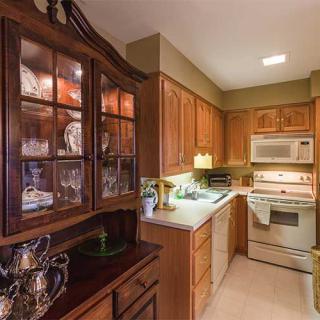 A cozy kitchen with wooden cabinets, featuring a microwave and oven, and glassware displayed in a cabinet.