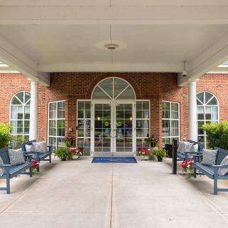 The entrance of a red brick building with a covered walkway and benches on either side.