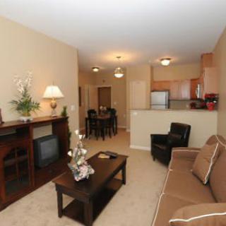 A cozy apartment living room with a sofa, coffee table, and a view into the kitchen and dining area.