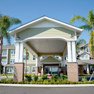 The entrance of a residential building surrounded by palm trees and well-maintained landscaping.