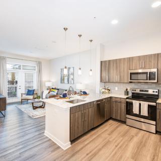 A modern open-concept kitchen and living area featuring wood flooring and stainless steel appliances.