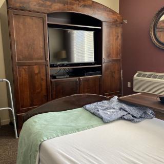A hospital room with a hospital bed, wooden wardrobe, and television.