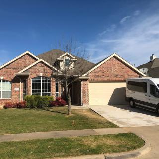 A suburban brick house with a van parked on the driveway under a clear blue sky.