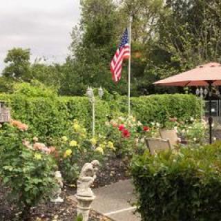 A lush garden with a variety of flowers, featuring an American flag and a cozy patio area under an umbrella.