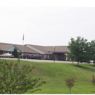 A view of a building with a lawn, trees, and parked cars.