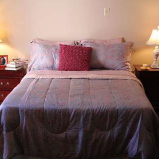 A cozy bedroom setup with a neatly made bed, accented by a red pillow and flanked by two bedside lamps.