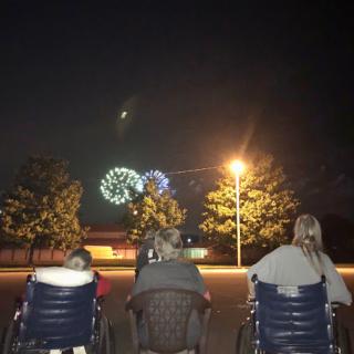 Three individuals enjoy a fireworks display under the night sky.