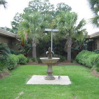 A serene garden featuring a central fountain surrounded by lush palm trees.