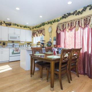 A cozy kitchen and dining area with wooden floors, featuring a dining table, white cabinets, and decorative curtains.