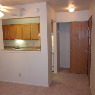 An apartment interior showing a small kitchen and hallway with warm lighting.