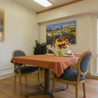 A cozy dining room with a table set for two, adorned with a bouquet of flowers and surrounded by comfortable chairs.
