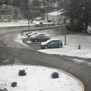 A snowy scene in a parking lot, with cars and a winding road.