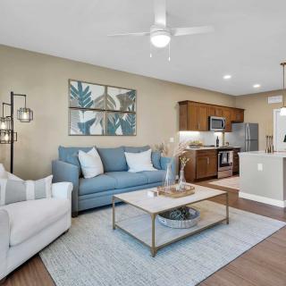 A modern living room with an open kitchen, featuring a blue sofa and a white armchair, accented by stylish decor.