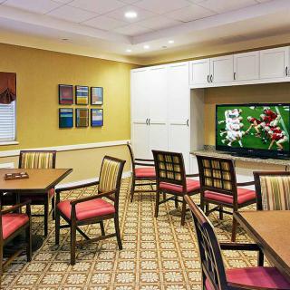 A meeting room with several chairs and tables, featuring a television displaying a sports game.