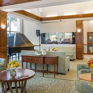 A cozy lounge area featuring elegant furniture, a grand piano, and a large aquarium.