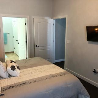 A minimalist bedroom with a bed, wall-mounted television, and open doors leading to an adjoining room.