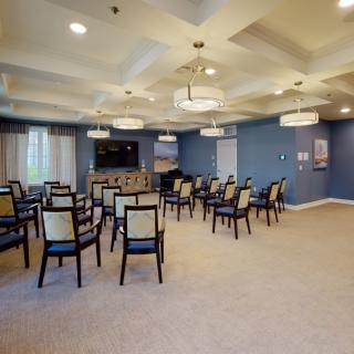 A neatly arranged conference room with chairs facing a television, featuring blue walls and stylish chandeliers.