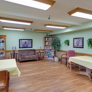 A cozy indoor space featuring comfortable seating, tables, and a bookshelf, illuminated by natural light.