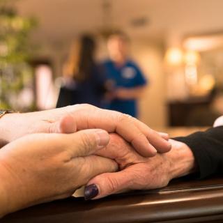A scene of care and compassion as two individuals hold hands in a supportive setting.