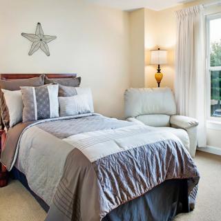 A cozy bedroom with a neatly made bed, a comfortable chair, and natural light coming through the window.