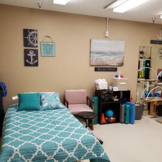 A cozy therapy room featuring a bed with teal accents, colorful decor, and organizational shelves.