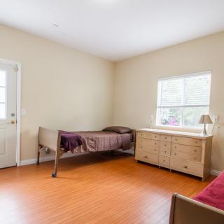 A simple bedroom with a single bed, dresser, and window letting in natural light.