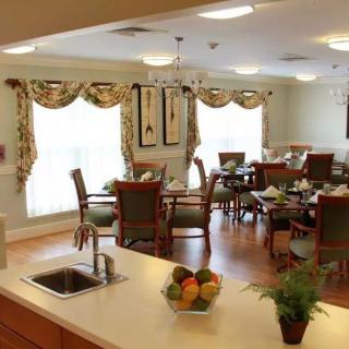 A well-lit dining room with elegant decor and neatly arranged tables and chairs, adjacent to a kitchen island.