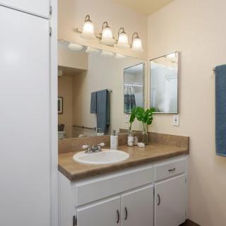 A tidy bathroom with a vanity, sink, and mirror, featuring modern lighting and neatly arranged towels.