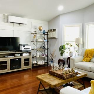 A cozy and modern living room with wooden flooring, featuring a television, bookshelf, air conditioner, and a chess board on the coffee table.