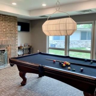 A cozy game room featuring a pool table, brick fireplace, and large windows.