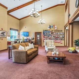 A spacious living room with high ceilings, featuring a sofa, armchair, and a coffee table, adorned with flags and decorations.