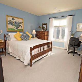 A cozy bedroom with blue walls, featuring a wooden bed frame, desk, and large window.