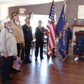 A group of veterans standing in an indoor setting, participating in a flag ceremony with American flags.