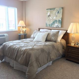 A cozy bedroom with a neatly made bed, decorative lamps, and artwork on the wall.