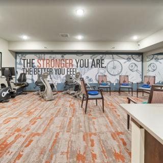 A fitness room with exercise equipment, chairs, and a motivational quote on the wall.