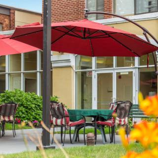 A cozy outdoor patio with tables and chairs under red umbrellas, located near a brick building.