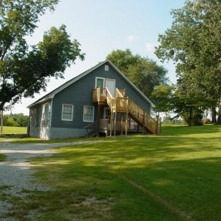 A gray house with a wooden staircase surrounded by trees and grass.